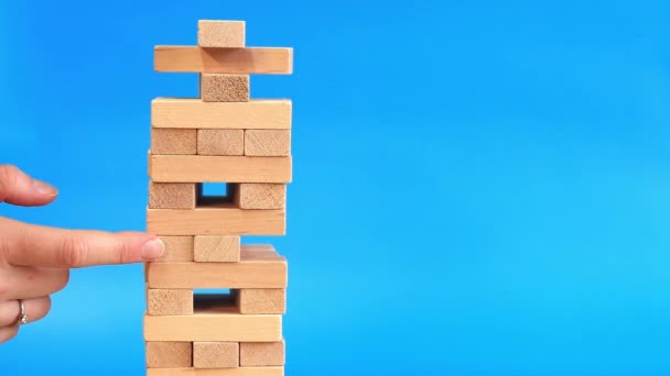 A woman plays Jenga on a blue bright background. The concept of family vacation, holidays, entertainment. A woman's hand takes out a block from a wooden toy tower. Game - Footage, Video