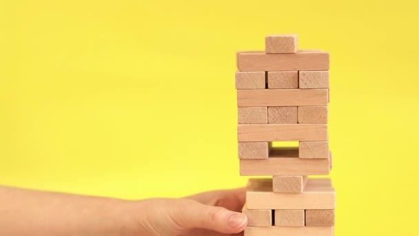 A woman plays Jenga on a yellow background. The concept of family vacation, holidays, entertainment. A woman's hand takes out a block from a wooden toy tower. A game - Footage, Video