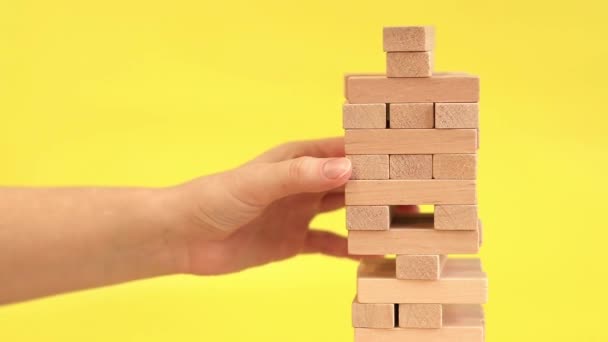 A woman plays Jenga on a yellow background. The concept of family vacation, holidays, entertainment. A woman's hand takes out a block from a wooden toy tower. A game - Footage, Video