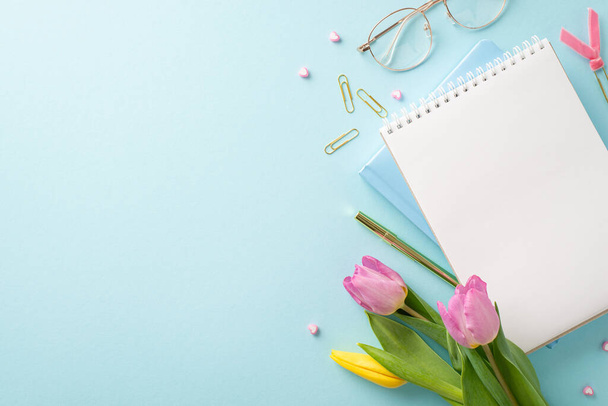 Professional Grace: Elevate Women's Day for the businesswoman. Top view of an office desk featuring classy glasses, notebooks, pen, clips, and tulips on a serene pastel blue surface - Photo, Image