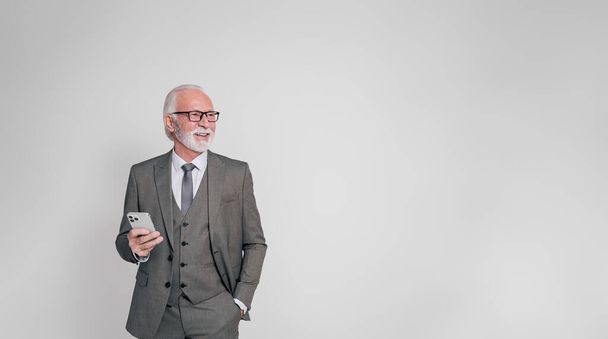 Šťastný senior podnikatel s rukou v kapse a mobilní telefon odvrací pohled přes bílé pozadí - Fotografie, Obrázek