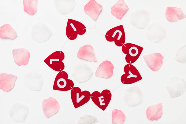 Garland červených srdcí na pozadí růžových okvětních lístků na Valentýna. Inscription love. Ruční práce. Plstěné výrobky. - Fotografie, Obrázek