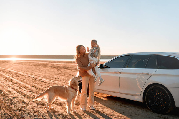 Madre con su hija y su perro cerca del coche al aire libre. Familia viajando con mascotas. Concepto de turismo, recreación y viajes. - Foto, imagen