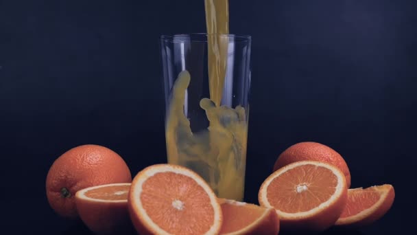 新鮮なオレンジジュースが黒い背景にガラスに注がれました. オレンジジュースには,繊維,ビタミンC,カルシウム,抗酸化物質が含まれており,消化および免疫システムを助けます. 健康的な飲酒のコンセプト。 スローモーション - 映像、動画