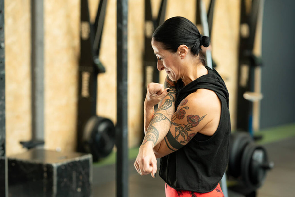 Side view of a mature strong woman with tattoos warming up in a cross training center - Photo, Image