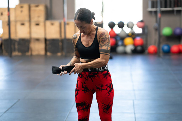 Mature modern woman with tattoos putting on a belt to prevent injuries while lifting deadlifts - Photo, Image