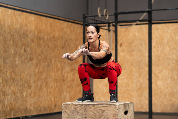 Horizontal photo with copy space of a tattooed woman exercising using box in a cross training gym - Photo, Image