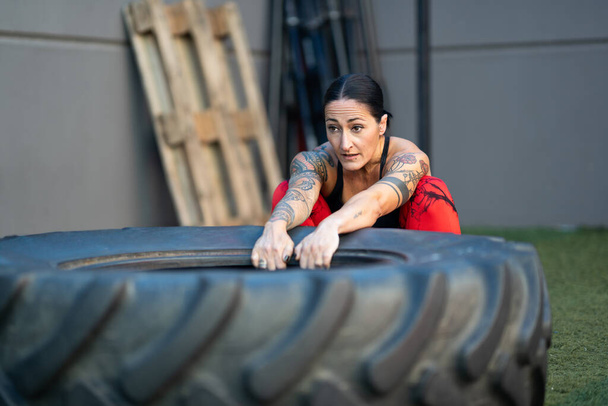 Strong mature woman about to flip a tire in a cross training gym - Photo, Image
