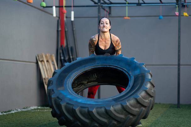 Frontal photo of a strong mature woman lifting a wheel in a gym - Photo, Image