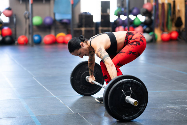 Horizontal photo of a sportive woman about to lift weight with bar in a gym - Photo, Image