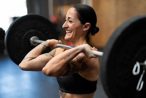 Close-up photo of a smiling mature woman lifting weights in a cross training gym - Photo, Image