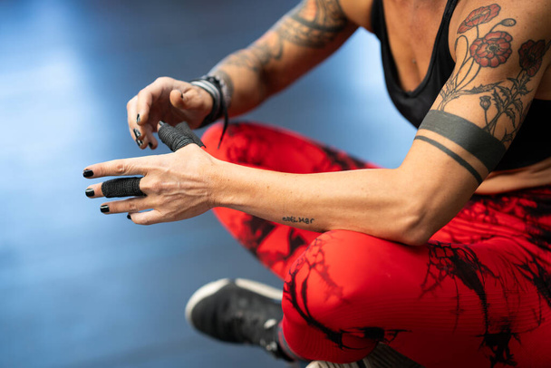 Close-up of athlete protecting her fingers with tape while sitting in the gym - Photo, Image