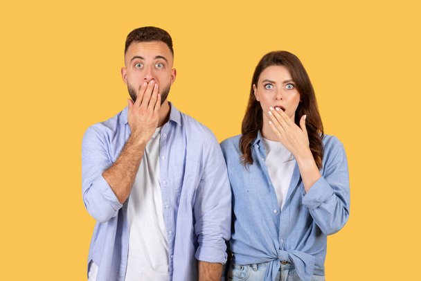 Hombre y mujer en ropa casual se cubren la boca con las manos, mostrando expresiones de asombro y sorpresa contra el fondo amarillo vivo - Foto, Imagen