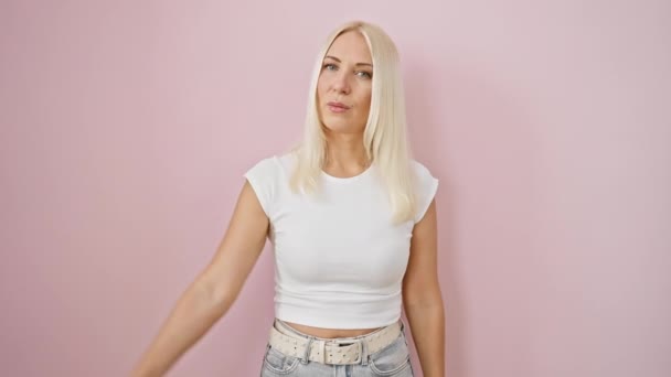 Wütende junge blonde Frau zeigt eine negative Daumen-nach-unten-Geste, sieht völlig unglücklich aus und pinkelt über isolierten rosa Hintergrund - Filmmaterial, Video