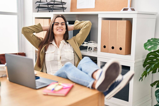 Young beautiful hispanic woman business worker relaxed with hands on head at office - Foto, Imagem