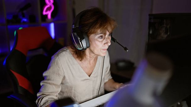Mujer madura juegos centrados en interiores por la noche usando tecnología de concentración de auriculares - Foto, imagen
