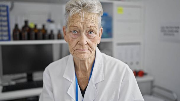 Laboratuvarda yüzü ciddi bir şekilde oturan kıdemli gri saçlı kadın bilim adamı. - Fotoğraf, Görsel