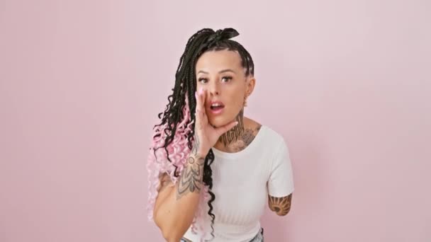 Femme amputée hispanique tatouée se tient sur fond rose isolé, couvrant la bouche à la main, chuchotant un secret intense, une conversation de commérages - Séquence, vidéo