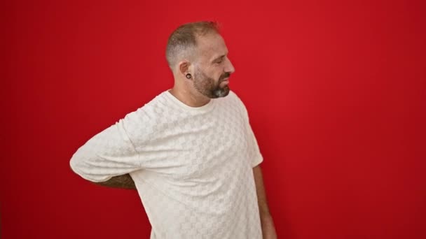 Jóképű, fiatal kaukázusi férfi komolyan szenved súlyos gerinc hátfájás, miközben áll aggódik egy elszigetelt vörös háttér fal - Felvétel, videó