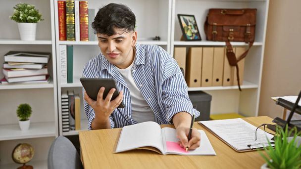 Un homme portant une chemise rayée prend des notes et voit une tablette dans un bureau à domicile avec une étagère et des plantes. - Photo, image