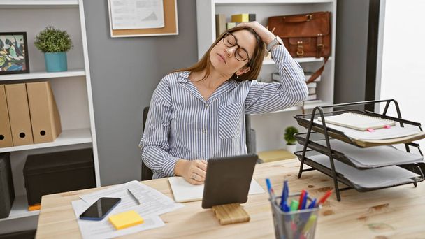 Eine müde junge Frau mit Brille an ihrem geordneten Schreibtisch. - Foto, Bild