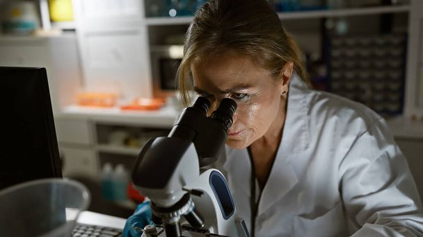 Rijpere vrouw wetenschapper met behulp van microscoop in laboratorium setting - Foto, afbeelding