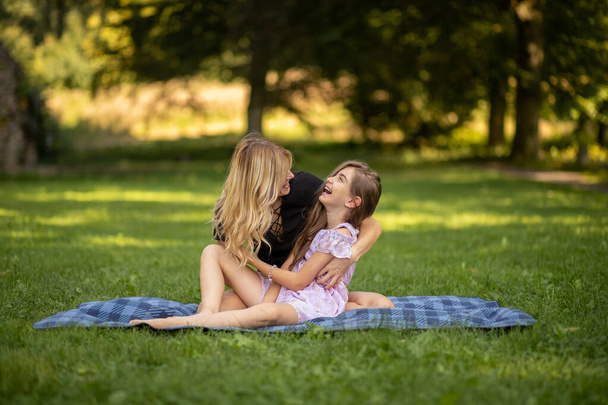 母と娘は抱擁し,笑い,ピクニックブランケットに横たわる. - 写真・画像
