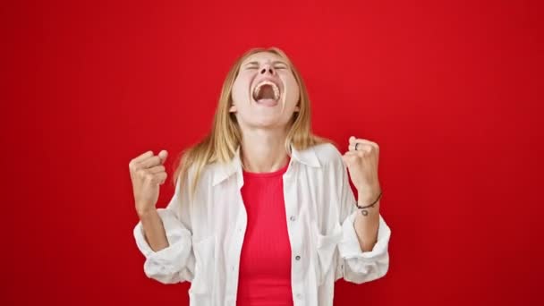 Een vrolijke blonde vrouw in een wit shirt over een rode top verrukt met een levendige rode achtergrond - Video