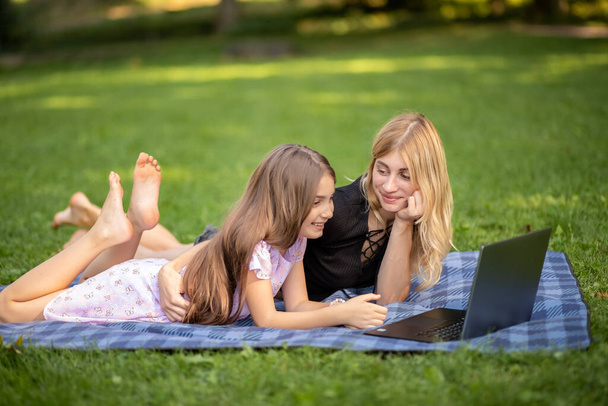 Madre e hija mirando un portátil mientras están acostadas en una manta. - Foto, Imagen