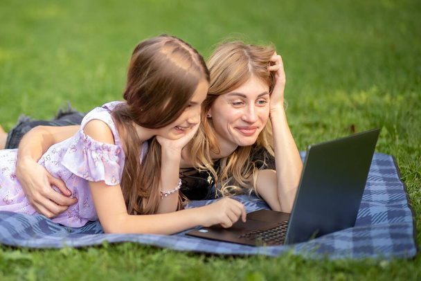 Mutter und Tochter schauen auf einen Laptop, während sie auf einer Decke liegen. - Foto, Bild