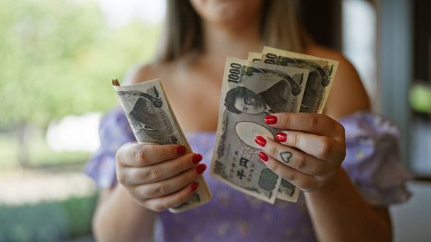 Смішна молода біла жінка, що рахує банкноти своєї японської єни, застрягла всередині ностальгічної кафетерії, займаючись розумними фінансовими рішеннями з її грошима в руці, підкреслюючи її багатство і багаті заощадження - Фото, зображення