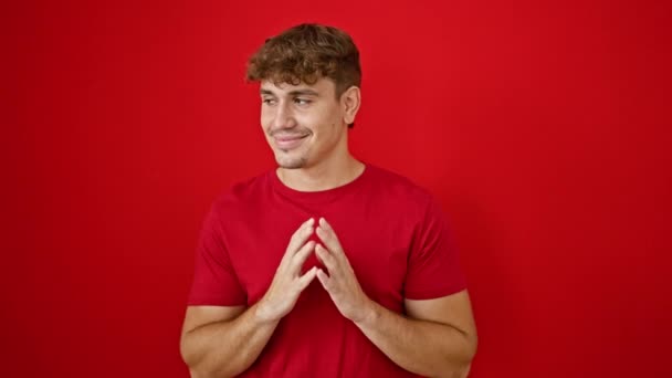Junger hispanischer Mann lächelt selbstbewusst mit zusammengelegten Händen vor isoliertem roten Hintergrund - Filmmaterial, Video