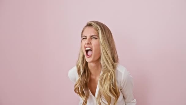 Young blonde woman screams in madness, frustration and rage, expressing powerful aggression and anger. wearing shirt, stands furious and upset isolated over pink background. raw emotion captured. - Footage, Video