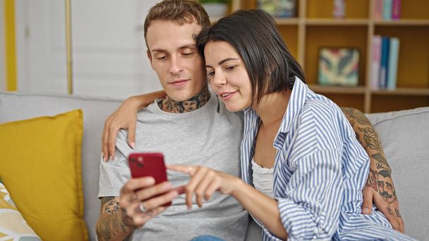 Beautiful couple sitting on sofa together using smartphone smiling at home - Photo, Image