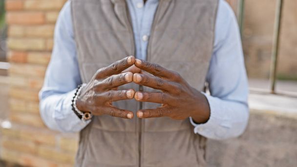 Gros plan sur les mains pliées d'un homme africain non identifiable avec un bracelet élégant, debout dans un cadre urbain. - Photo, image