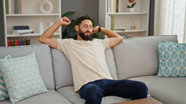 Giovane uomo ispanico seduto sul divano stanco braccia tese a casa - Foto, immagini