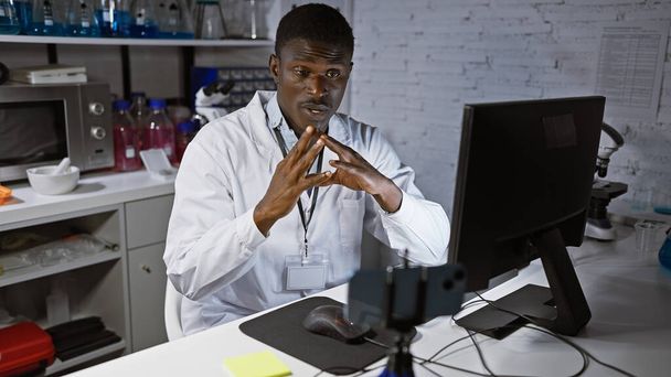 Un uomo africano concentrato in un camice da laboratorio che analizza i dati su un computer in un moderno ambiente di laboratorio. - Foto, immagini