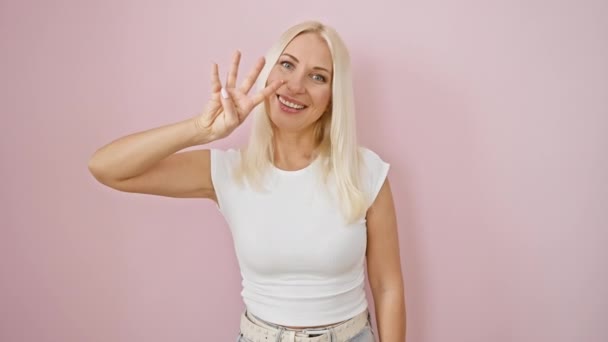 Vrolijke jonge blonde vrouw vol vertrouwen uitdrukken van de nummer vier, wijzen met de vingers tijdens het staan, alle glimlacht over een roze geïsoleerde achtergrond. - Video