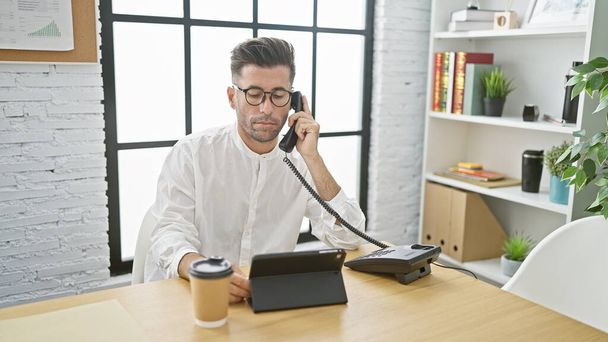 Νεαρός Ισπανός επιχειρηματίας που μιλάει στο τηλέφωνο και εργάζεται στο γραφείο - Φωτογραφία, εικόνα
