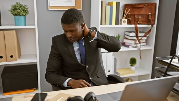 Красивий африканський чоловік у костюмі відчуває біль в шиї під час роботи в сучасному офісі. - Фото, зображення