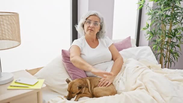 Selbstbewusste Frau mittleren Alters im Pyjama mit grauhaarigem Hund, die auf ihrem Bett sitzend eine defensive Stoppgeste macht und in der Abgeschiedenheit ihres Schlafzimmers einen ernsten Ausdruck anbietet. - Filmmaterial, Video