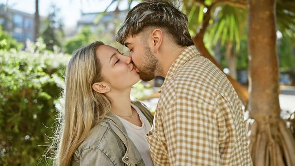 Kochająca się para całująca się na świeżym powietrzu otoczona zielenią w słonecznym parku, przywołująca romans i intymność. - Zdjęcie, obraz