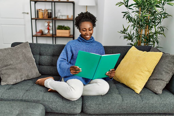 Afroamerykanka czyta książkę siedząc na kanapie w domu - Zdjęcie, obraz