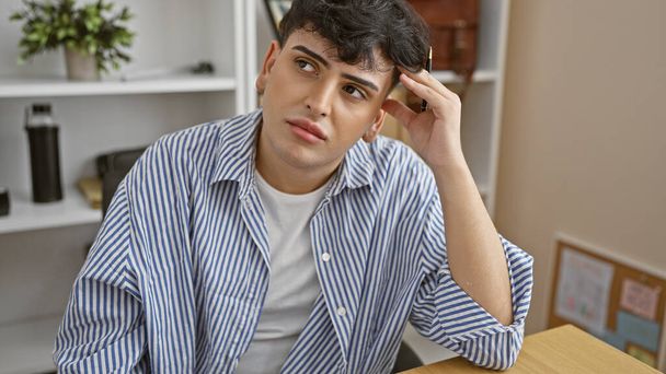 Pensive fiatal férfi irodai környezetben csíkos ing megható haj és szemlélődő megjelenés. - Fotó, kép