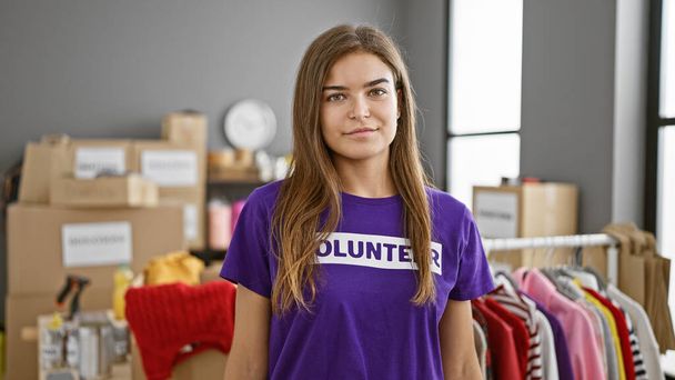 Fiatal gyönyörű spanyol nő önkéntes áll komoly arccal jótékonysági központ - Fotó, kép