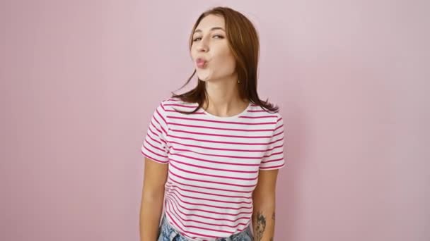 Schattige jonge brunette in een gestreept T-shirt, die een leuke airborne kus naar de camera blaast, uitingen van liefde en positieve energie stuurt. een verbluffend casual zicht over een roze geïsoleerde achtergrond. - Video