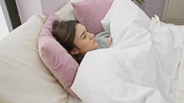 Μια νεαρή Ισπανίδα ξαπλωμένη στο κρεβάτι με λευκά λινά σε ένα άνετο υπνοδωμάτιο. - Πλάνα, βίντεο