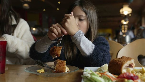 Kleines Mädchen isst Essen im Restaurant, Kind genießt Cordon bleu Huhn für die Mahlzeit im gemütlichen Holzinterieur. Familie beim Abendessen - Foto, Bild