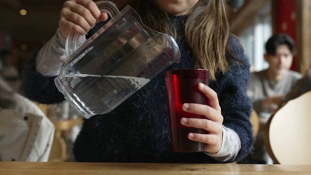 レストラン内で瓶を保持することによってカップに水を供給する小さな少女 - 写真・画像