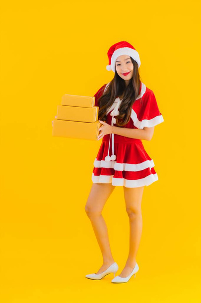 Portrait beautiful young asian woman wear christmas clothes hat with parcel box packaging ready for shipping on yellow isolated background - Photo, Image